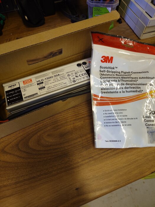 Nätaggregat från MW i kartong och en förpackning med 3M Scotchlok självskärande pigtail-kontakter på ett träbord.