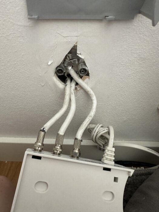 Antennuttag med flera anslutna kablar och en borttagen kåpa på väggen. Kablarna går nedåt, potentiellt tidigare kopplade till takantenn.