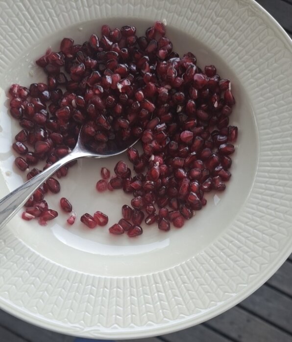 Granatäppelkärnor i en vit skål med en sked, serveras som efterrätt.