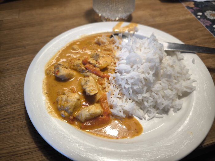 Tallrik med panengcurry innehållande kyckling och ris på ett träbord.