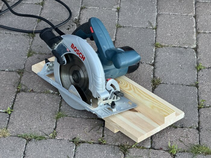Cirkelsåg från Bosch placerad på marksten bredvid en träbit, redo för användning i ett byggprojekt.