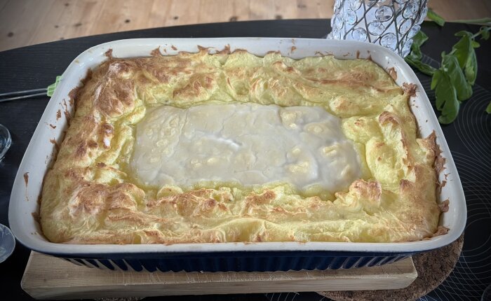 Laxgratäng med hemstompat potatismos och vitvinssås i en ugnsform på ett bord.