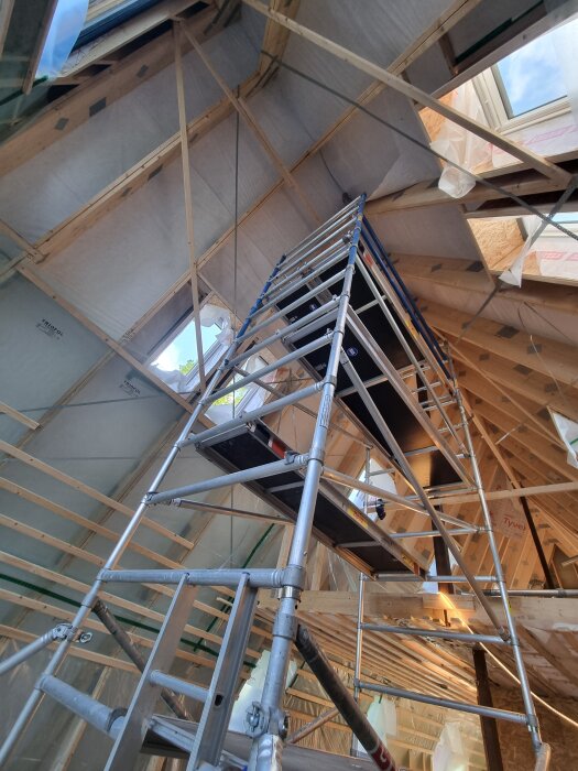 Byggnadsställning inuti en nästan färdig vindsvåning med träbjälkar och ljusinsläpp från takfönster.