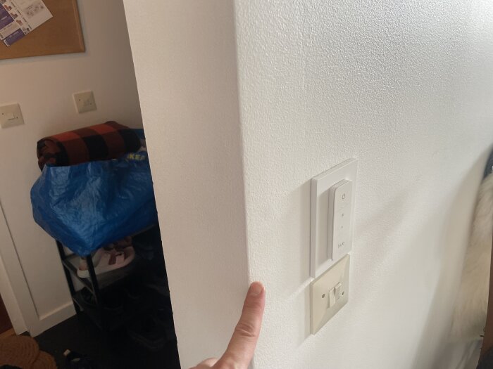 Vägg med två strömbrytare och en person som pekar på platsen. En hylla planeras monteras på andra sidan väggen.