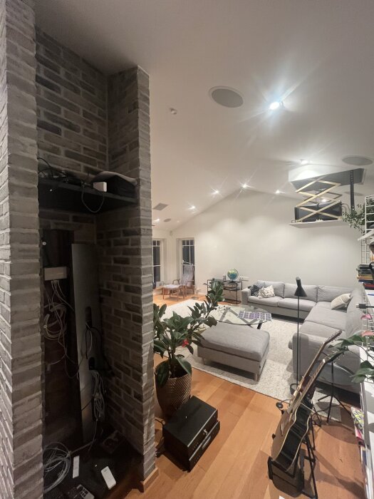 Hemmabiorum med modern inredning, kablar vid öppen murad vägg, utrustning för AV-system på golvet, gitarr i stativ och grå soffa i bakgrunden.