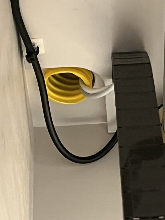 Svart kabel och vit kabel som går in i en gul kabelkanal på en vit vägg, del av hemmabioinstallation.