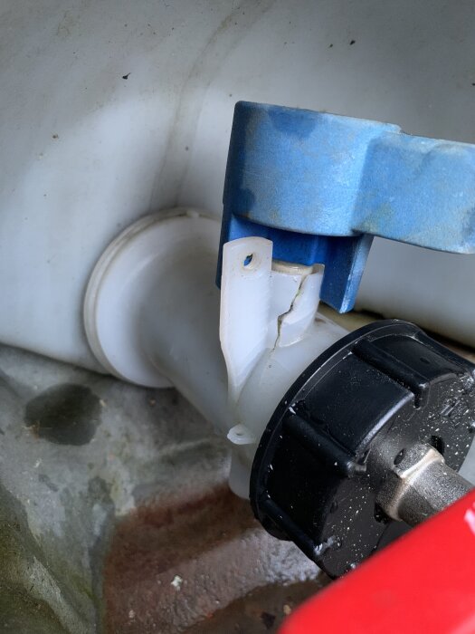 Trasig vit plastkomponent med blå och svart fäste, del av ett rörsystem, fotograferat inuti ett trångt utrymme.