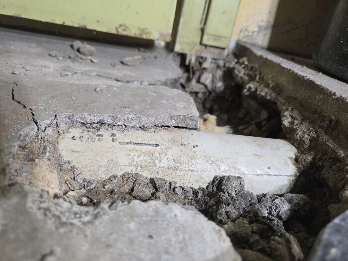 Närbild på ett blottlagt avloppsrör under en sprucken betongplatta, del av ett renoveringsprojekt.