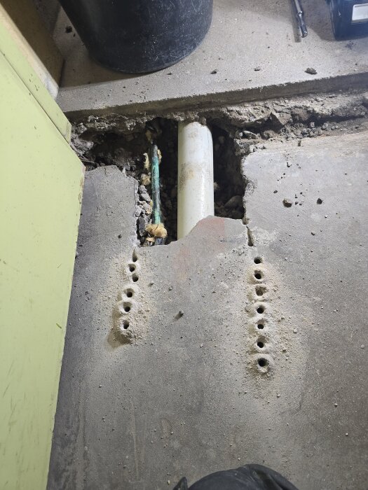 Bilden visar en del av ett betonggolv där hål är borrade och ett avloppsrör är frilagt i ett garageprojekt.