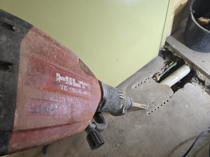 Hilti TE 1500-AVR bilmaskin bryter upp betonggolv för att exponera ett avloppsrör, under en renovering i ett garage.