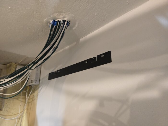 Flera kablar är dragna genom ett hål i taket och de hänger ner längs en vit vägg där en montagelist är fastskruvad.