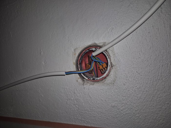 Elinstallation i vägg med exponerade kablar och kopplingskontakter i en öppen dosa, mot en vitmålad väggyta.