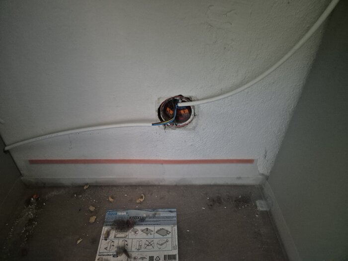 Vägg med ett montagehål där elkablar och ett eluttag syns, kabeldragning sticker ut till vänster. Elektriska anslutningar synliga.