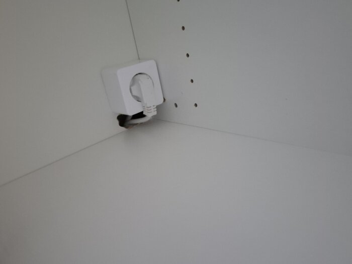Eluttag monterat på tunn MDF-skiva i skåp. Synlig kabelinstallation och hål i väggen. Fråga om korrekt montering och dolt fel vid bostadsköp.