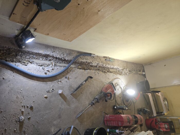 Bild av ett golv med uppbruten betong där gamla avloppsrör är borttagna. Verktyg och strålkastare syns runt omkring.