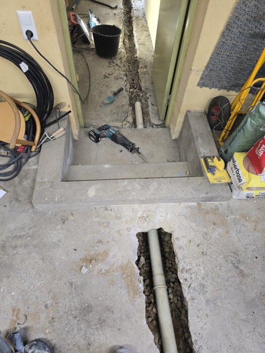 Upprivet golv med avloppsrör synliga i ett rum under renovering, verktyg och material runtomkring.