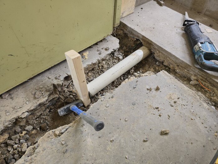 Uppbruten betonggolv med synligt plasströr, timmer och verktyg; en del av ett avloppsrenoveringsprojekt.