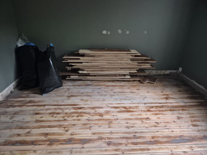 Rum i renovering med staplade golvplattor och sopsäckar mot väggen.