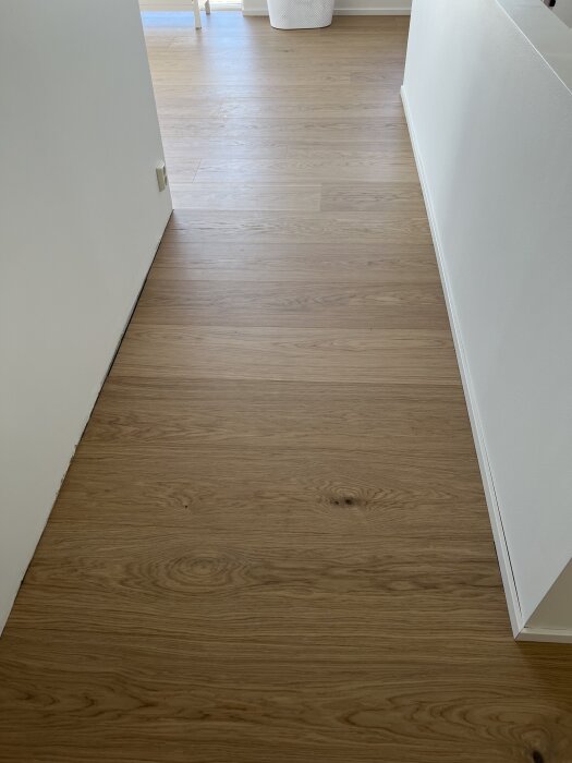 Golvet på övervåningen med nylagd parkett som visar en lutning mot rummets mitt, synligt från trappans räcke till motsatta väggen.