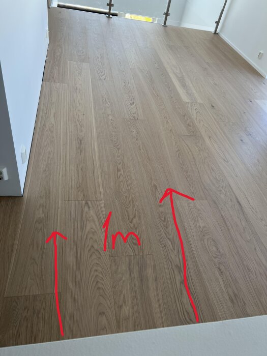 Golvet i ett tvåvåningshus visar en lutning med röda pilar och måttet 1 m markerat på trägolvet nära en trappa.
