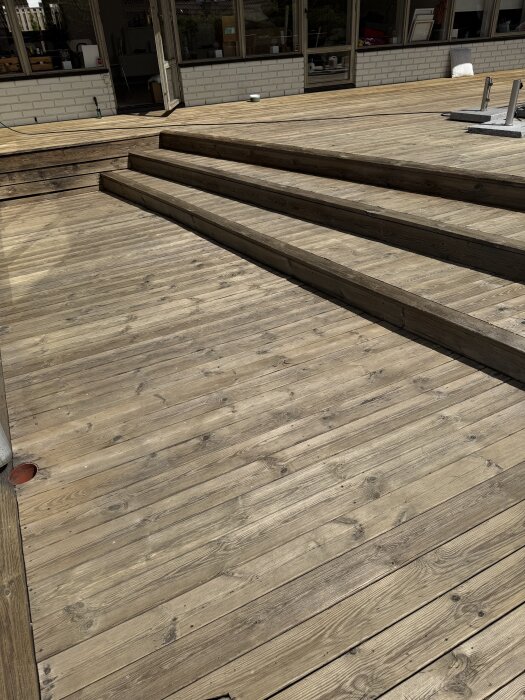 Nyrengjord altan i trä med tre steg, belyst av solsken, med en gulaktig nyans efter behandling med rengöringsmaskin och Cuprinol Tralltvätt.