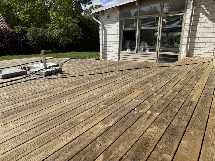 Nyrenoverad altan i gult och beige, belägen vid ett hus med vit tegelvägg och stora fönster, badar i solsken.