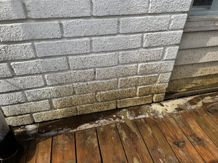 Fasad och altan med smuts och vattenstänk efter rengöring, synlig brädstruktur och vitmålad enkel tegelyta med mörkare nyans längst ner.