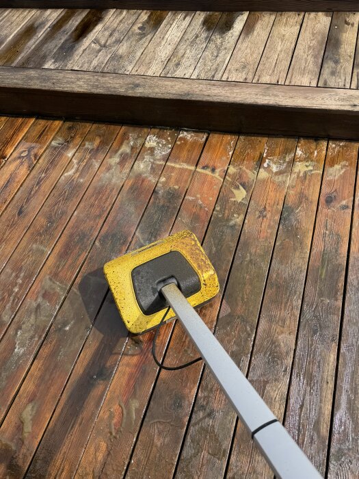 Gul altantvättmaskin på trätrall, rengöring av smutsig altan, ändrar färg från mörk till ljusare ton.