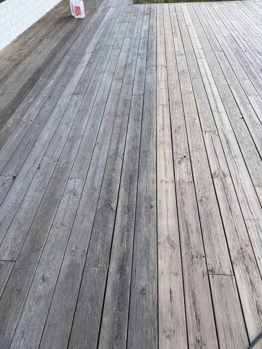 Före och efter rengöring av altan: vänster sida är grå och smutsig, höger sida är rengjord och har en ljusare träton.