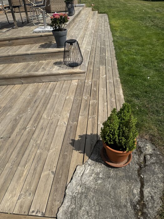 Nyrenoverad altan med trätrall, delvis i skugga. En blomkruka och en ljuslykta av metall står på trallens steg. Gräsmatta i bakgrunden.