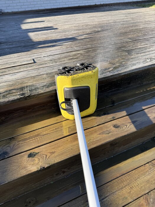 Gul Kärcher PCL 6 maskin används för att rengöra en träaltan, med vattenstrålar synliga mot de smutsiga brädorna.