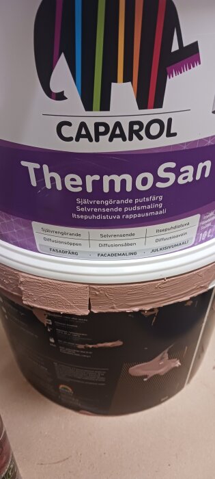 Färgbehållare med etiketten "Caparol ThermoSan" på en arbetsyta, visar läckande färg på sidan av burken.