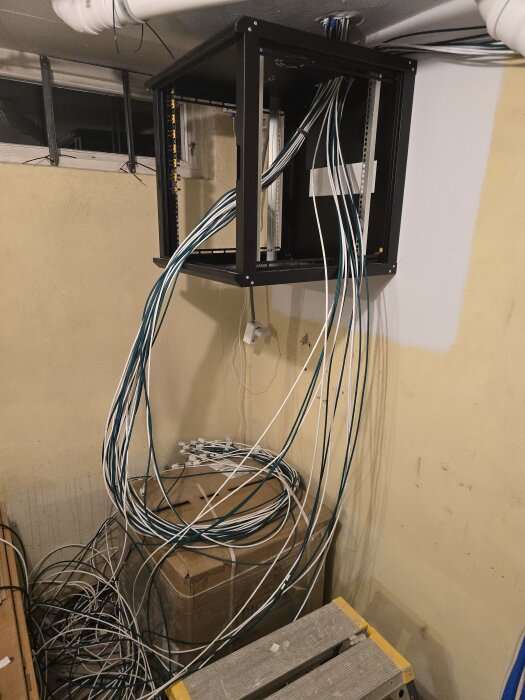 Hängande nätverksrack med många kablar som löper nedåt, oredigt längs vägg och golv, i ett rum under renovering.