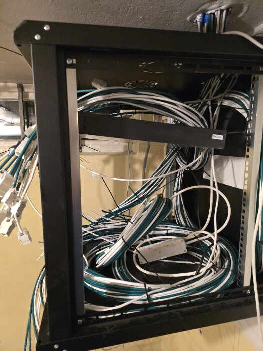 Bild av ett nätverksrack med ett stort antal vita och blå kablar hängande och upplindade inuti, många utan modularkontakter.