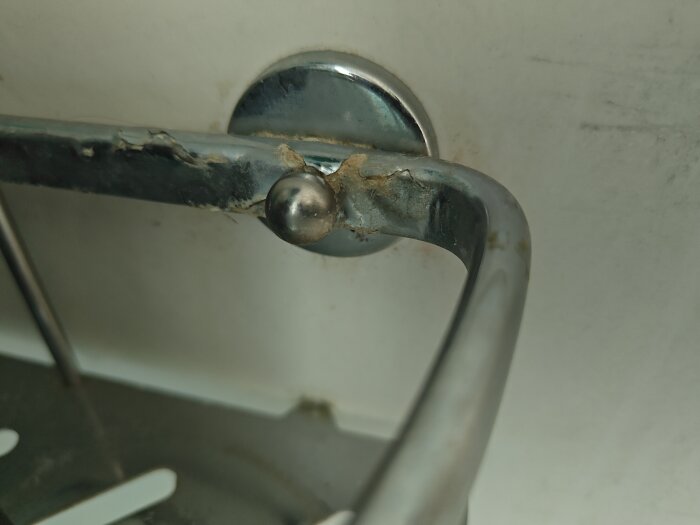 Metallhylla fäst på kakelvägg i dusch, eventuellt limmad.