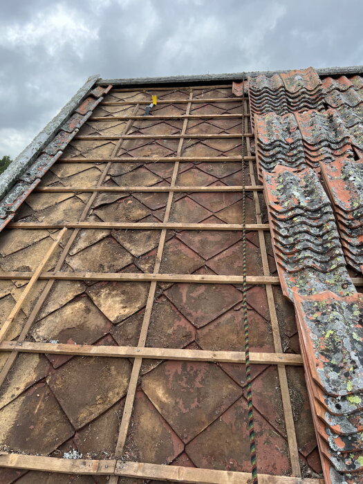 Tegeltak med masonit-diagonaler och öppna takstolar, delvis avbruten högerkant med travade tegelpannor, under byte eller renovering.