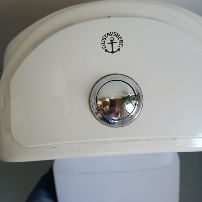 Vit cistern med en Gustavsberg-logotyp och en rund spolknapp i krom.