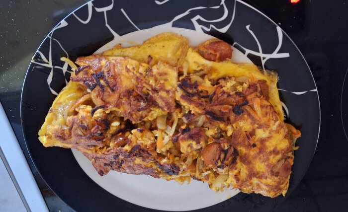 Omelett med rå potatis, morot, lök och ägg på en svartvit tallrik.