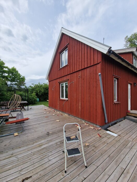 Rött hus på en nybyggd altan med en stege i förgrunden och träspill runt.