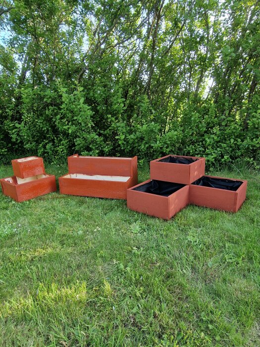 Hemgjorda blomkrukor av spillvirke i rostbrun färg står på en gräsmatta framför en grön häck.