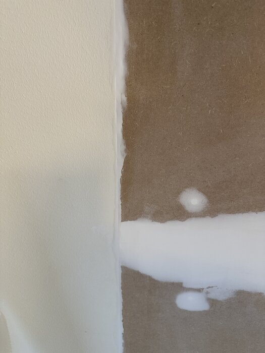 Glipan mellan mdf-skiva och vägg är tätad med vit akrylfog, synlig från sidan med slipade och ojämna kanter.