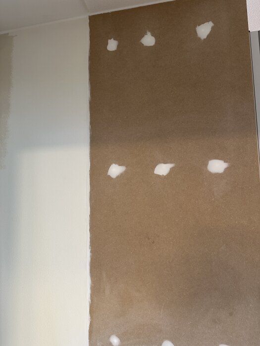 MDF-skiva monterad på vägg med akrylfog fylld i skruvhålen, ansluten till en garderob. Glipa tätad med fog, försök till slipning.