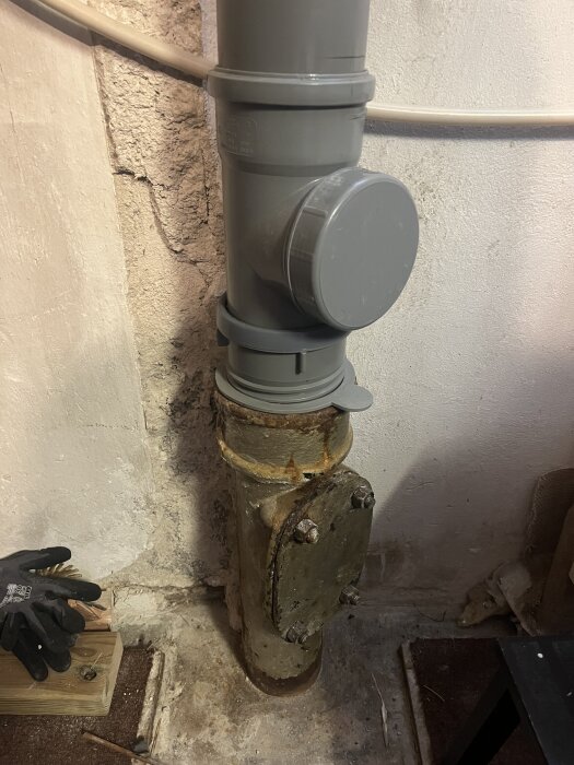 Grå Faluplast expanderrör monterat på ett gammalt rostigt rör i källaren, med en handske liggande vid sidan.