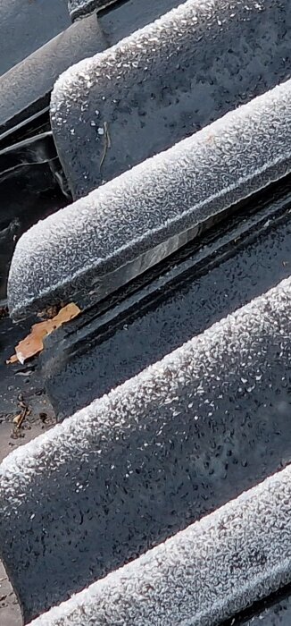 Närbild av ett tak där det syns en glipa mellan takpannorna efter omläggning, delvis täckt av frost och några löv.
