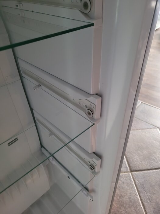 Invändigt skadat kylskåp med glas hyllor och plast som bucklar ut.