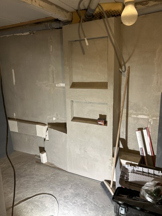 Inbyggd rörstam i badrum med exponerade rör, omgivna av byggmaterial och verktyg. Diskussion om renslucka för underhåll.