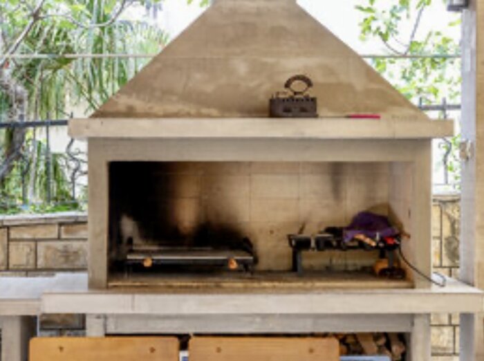 Utomhusmurad grill med sluttande tak och öppning; insidan har en grillplåt och föremål vid sidan.