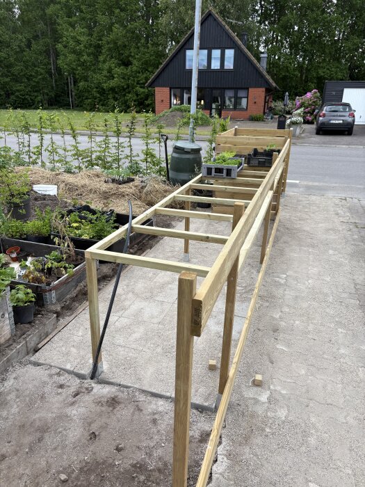 Ram av tryckimpregnerat virke för ett utomhusplanteringsbord utan plank på sidor och baksida, placerat vid en uppfart nära en trädgård.