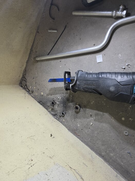 Verktyg som skär igenom rör och material i ett renoveringsprojekt, med avklippta rör och kabelrester på golvet.