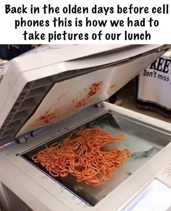 Spaghetti med tomatsås ligger på glaset i en öppen kopieringsmaskin. Text ovanför beskriver hur man tog bilder av lunch "förr i tiden".
